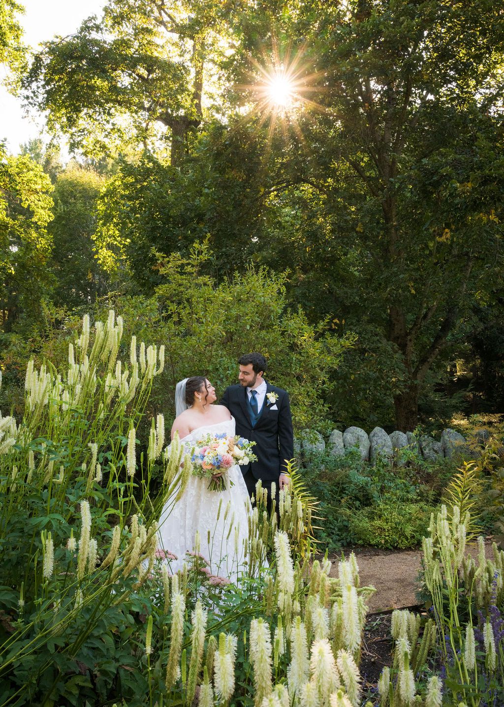 Sunlight streams through trees in a garden filled with white flowering plants creating a magical wedding scene.