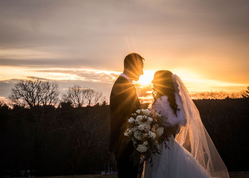 A romantic sunset silhouette of a couple in wedding attire embracing against a golden sky.