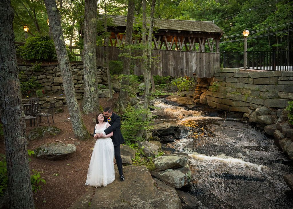 A wedding couple poses on natural stone formations surrounded by lush forest greenery.