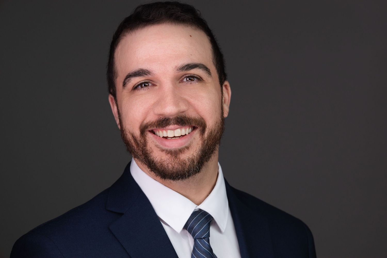 Professional headshot portraits of person in business attire against dark background showing different expressions.