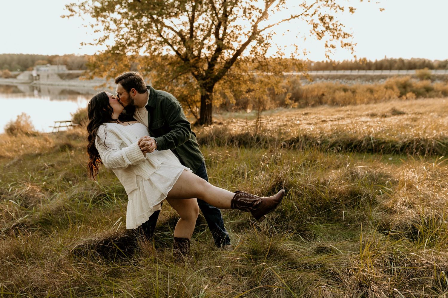 A romantic couple embraces in a sunny field during golden hour.