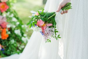 Close-up of bride holding fresh spring bouquet with white dress in background.
