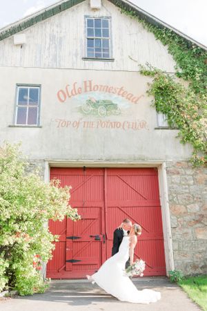 Rustic barn wedding venue with red doors and 'Olde Homestead' signage on white facade.