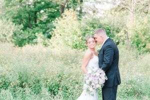 A wedding couple shares an intimate moment in a sunlit meadow with soft pastel florals.