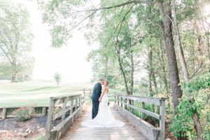 Ethereal wedding photo on rustic wooden bridge surrounded by lush greenery.
