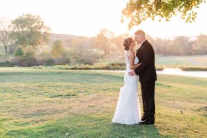 Newlyweds embrace during golden hour in an outdoor countryside setting.