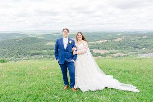 A couple embraces on a scenic hilltop overlooking rolling green countryside on their wedding day.