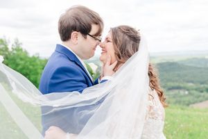 Newlywed couple shares romantic moments in a lush green mountain landscape with flowing white veil in the breeze.
