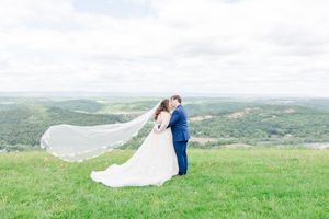 A couple shares a romantic moment on a grassy hilltop with a sweeping mountain landscape in the background.