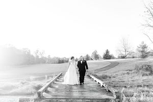 A black and white photo shows a couple walking down a misty boardwalk path through a natural landscape.