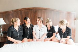 A group of five friends in matching pajamas sit together on a bed while sharing a laugh.