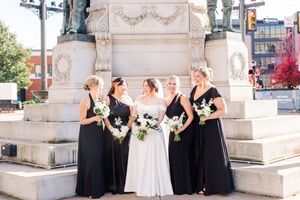 Wedding party poses and celebrates in front of elegant white stone architecture with ornate details.
