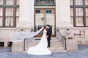 A bride and groom share a romantic moment between elegant white columns of a historic building.