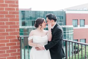 A romantic couple embraces during their wedding photoshoot on a rooftop terrace with red brick walls.