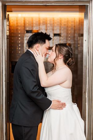A bride and groom share a romantic kiss in front of a warmly lit window display at their wedding.