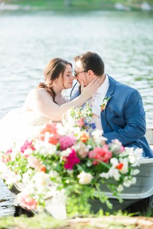 Romantic wedding couple embrace near water with colorful floral arrangements.