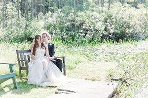 A couple shares a romantic moment on a wooden bench surrounded by lush greenery in an outdoor garden setting.