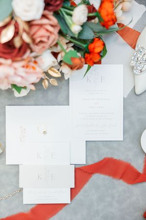 Wedding stationery and invitations arranged with coral ribbons and pink floral accents on gray surface.