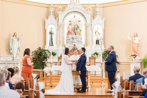 Wedding ceremony inside an elegant white church with ornate architectural details and religious statues.