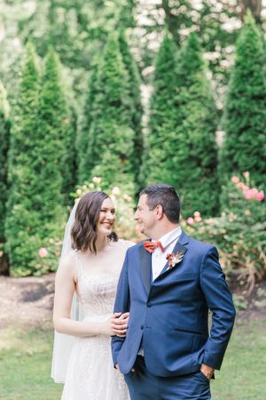 A couple shares a romantic moment in a garden setting with evergreen trees in the background.