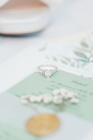 A sparkling diamond engagement ring rests on a soft mint green wedding invitation with delicate details.