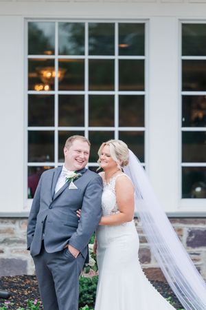 A happy couple shares a joyful moment together during their outdoor wedding celebration in front of a windowed building.