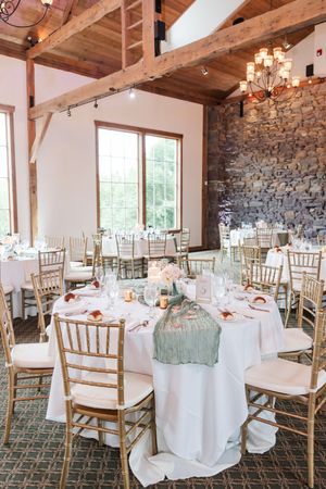 Elegant wedding reception venue with rustic stone walls, exposed wooden beams, and round tables set with mint linens.