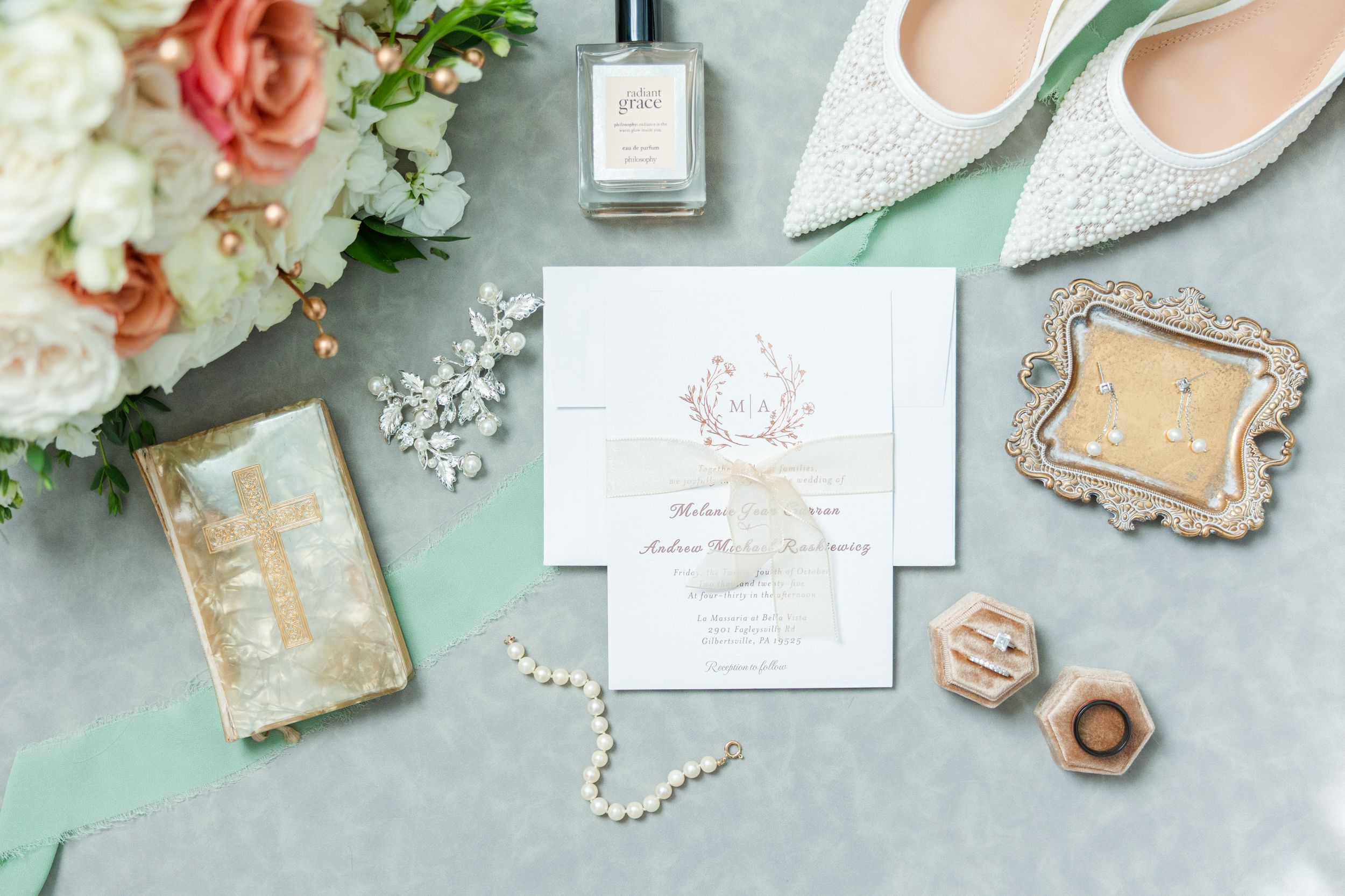 Flat lay of wedding accessories including pearl necklace, floral decor, invitations, and delicate shoes on mint background.