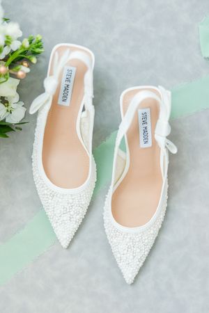 Elegant white beaded slingback bridal shoes with pointed toes displayed on light gray and mint green background.