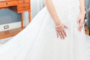 A person in a white wedding dress with a flowing skirt stands gracefully against a light-colored background.