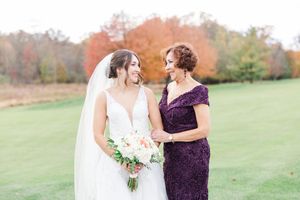Two women in formal dresses walking together through an autumn field during a wedding celebration.