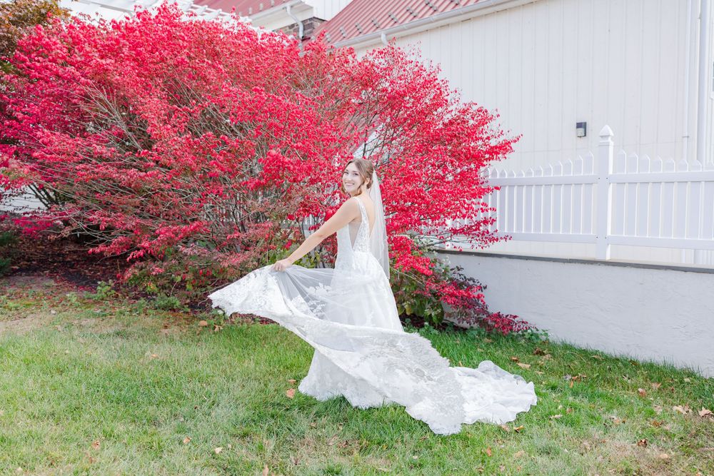 White wedding dress flowing in front of a white fence with vibrant red autumn foliage in the background.