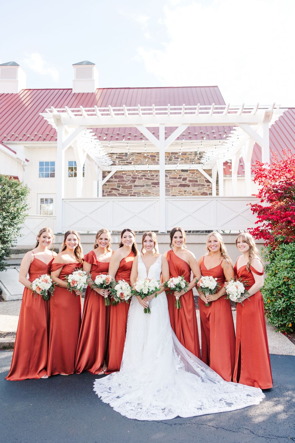 Wedding party in burgundy bridesmaid dresses and white bridal gown pose together outdoors in autumn setting.