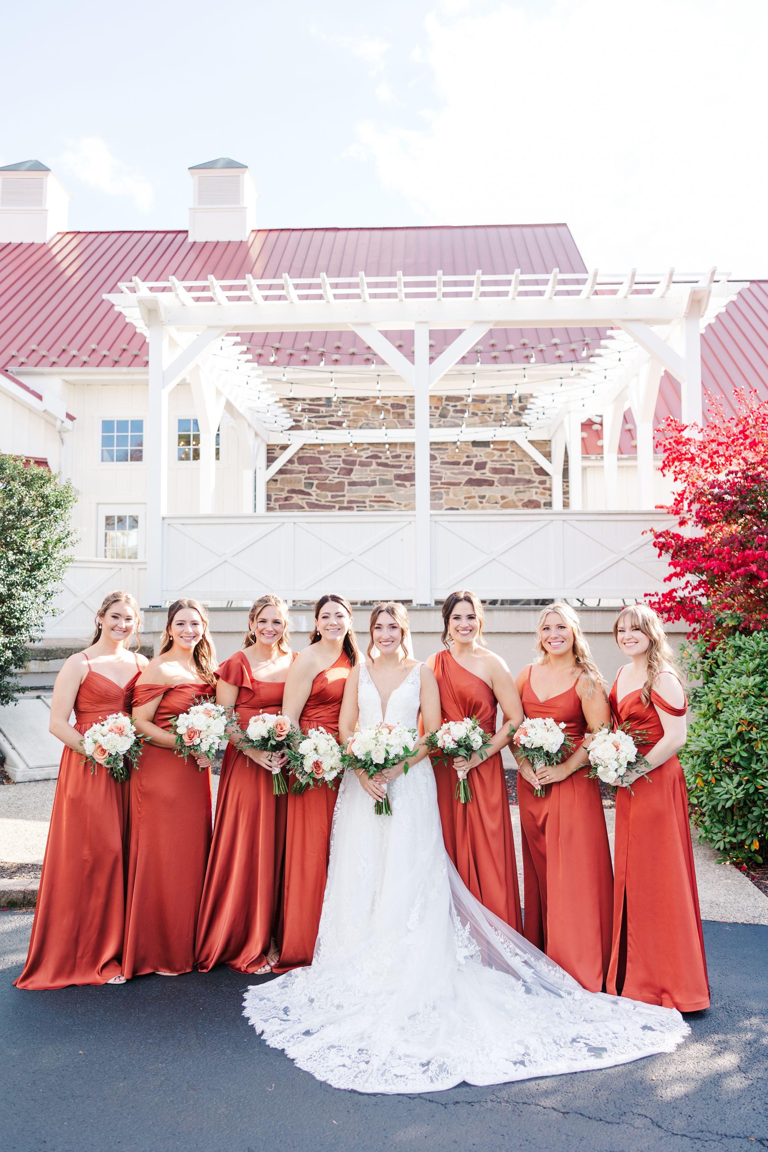 Wedding party in burgundy bridesmaid dresses and white bridal gown pose together outdoors in autumn setting.