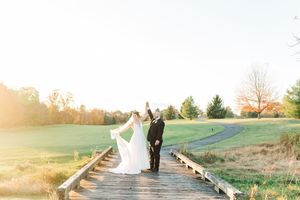 Newlywed couple walking on wooden boardwalk at sunset with green golf course in background.