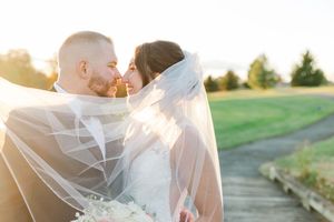 Romantic sunset wedding portrait of couple embracing on wooden path with veil flowing in breeze.