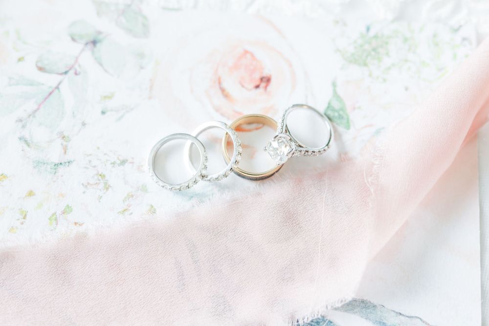 Three elegant wedding rings arranged on delicate pink fabric with floral pattern.