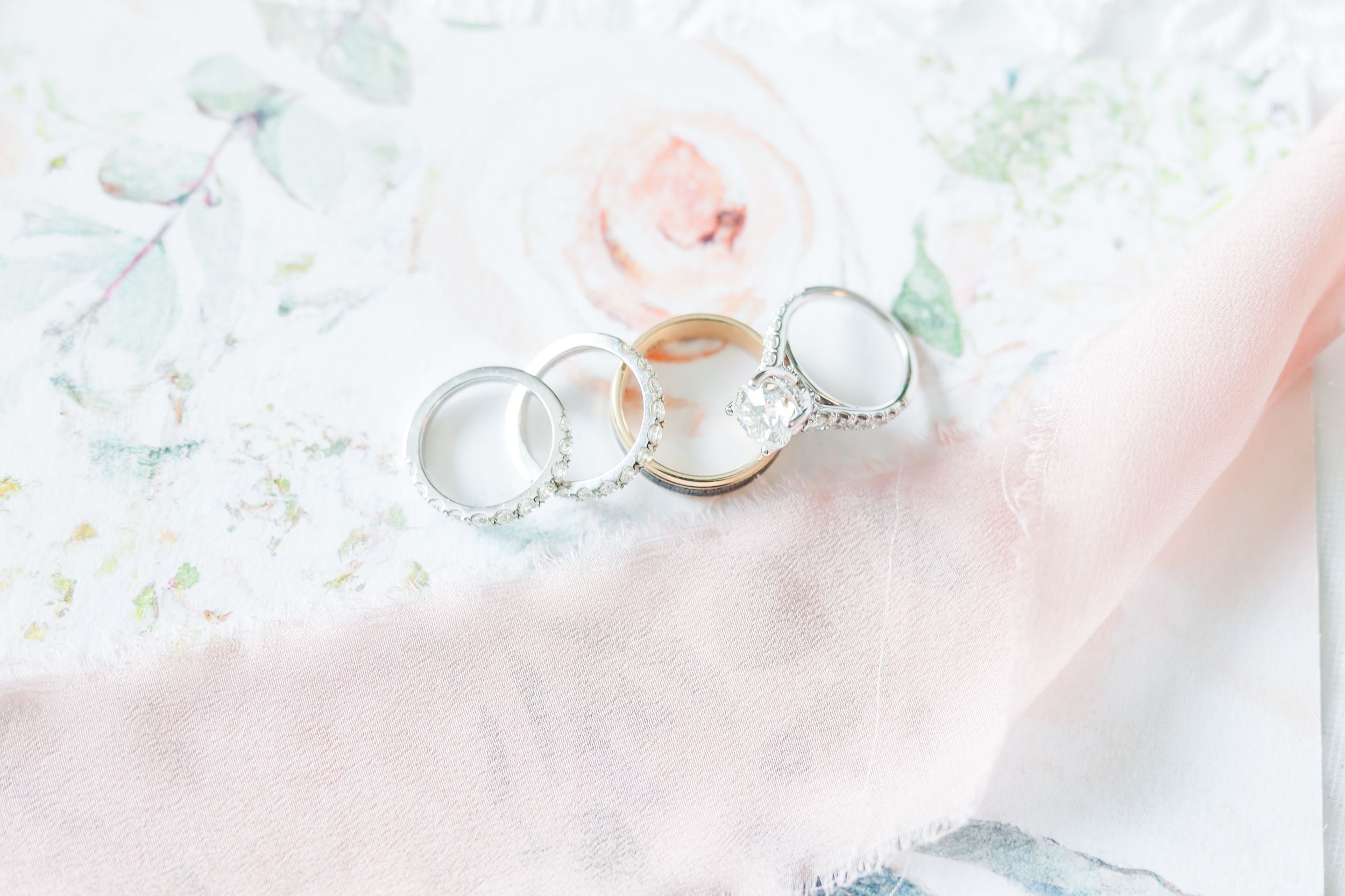 Three elegant wedding rings arranged on delicate pink fabric with floral pattern.