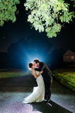 Dramatic nighttime wedding portrait under tree branches with blue backlight creating magical atmosphere.