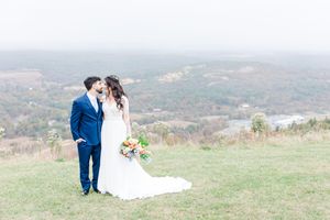 A couple in wedding attire shares a romantic moment on a hilltop overlooking a scenic mountain landscape.