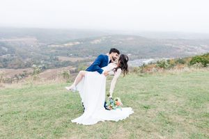 A romantic wedding couple embraces on a hilltop overlooking a scenic valley landscape during golden hour.