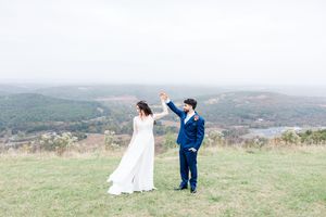A couple in wedding attire stands on a scenic hilltop overlooking a vast green landscape on their special day.
