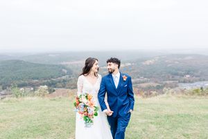 A couple in wedding attire stands together in a scenic mountain landscape with autumn colors in the background.