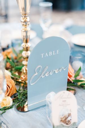 Elegant wedding table decor with light blue table numbers and peach roses against a soft focus background.