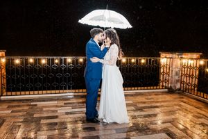 A romantic rainy wedding photo series showing a couple dancing and embracing under an umbrella with string lights glowing.