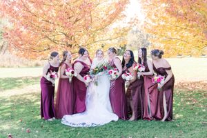 Bridal party in burgundy dresses poses together under vibrant fall foliage.