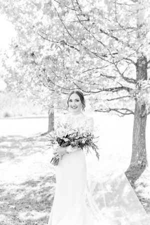 Black and white portrait of bride holding bouquet under blooming spring tree.