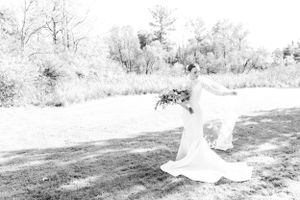 Black and white artistic portrait of bride twirling in elegant wedding dress outdoors.