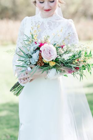 An elegant bridal bouquet with pink roses, greenery and wildflowers against a white wedding dress.