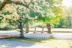 Elegant outdoor wedding venue with wooden arch and white chairs set up under flowering trees.